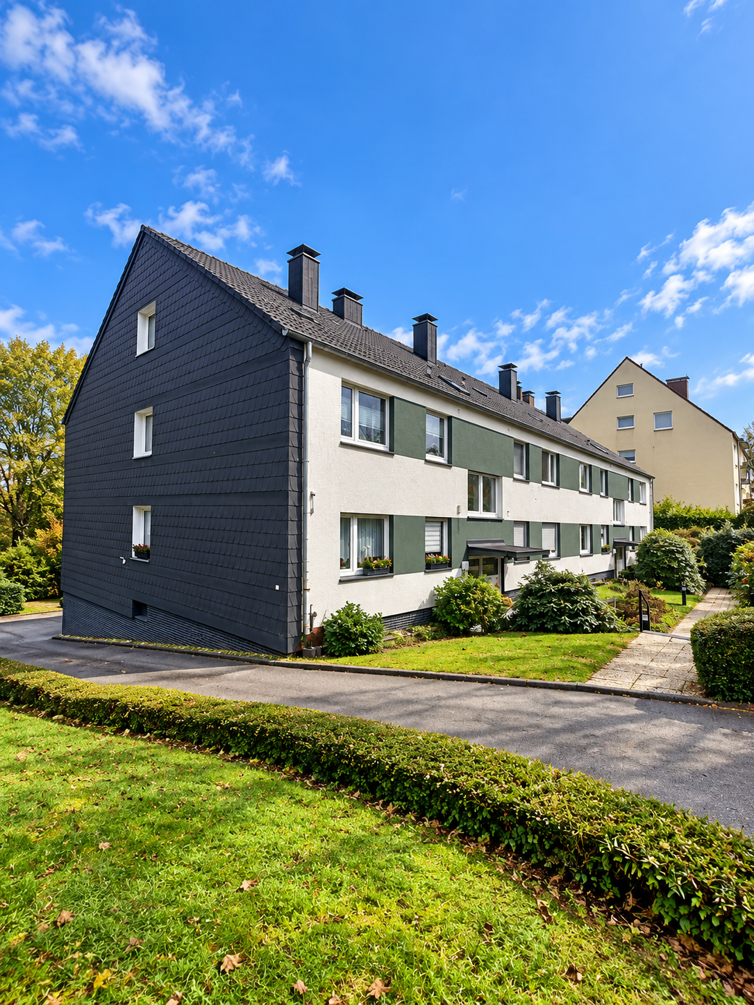 Wohnhaus Echoerstr. 53/55 mit heller Fassade, dunklem Giebel und begrünten Außenanlagen